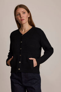 Woman wearing M.PATMOS Selena Ribbed Cardigan in Black. A v-neck cotton silk sweater with pockets.