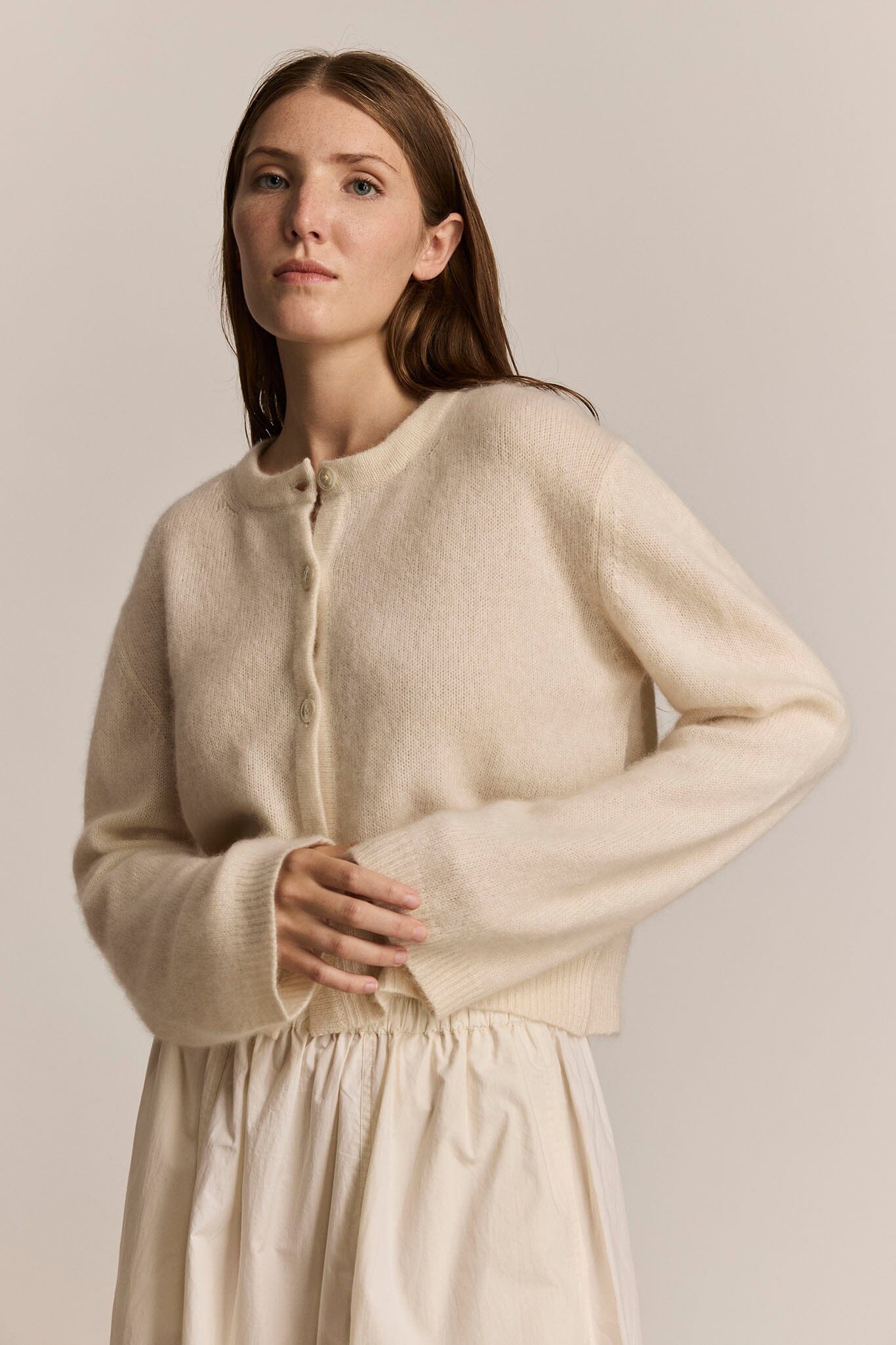 Woman wearing a long sleeve cashmere ivory sweater against a plain background