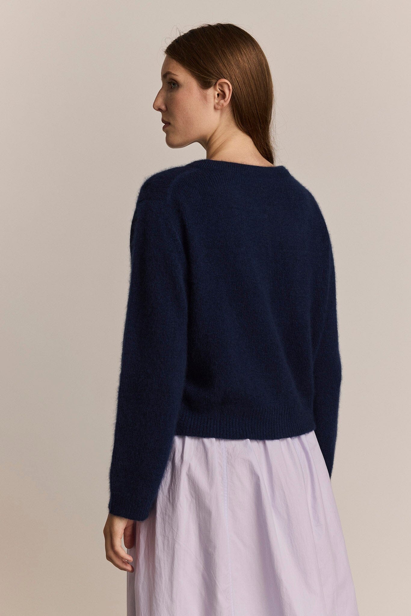 Woman wearing a navy blue sweater and light purple skirt against a beige background