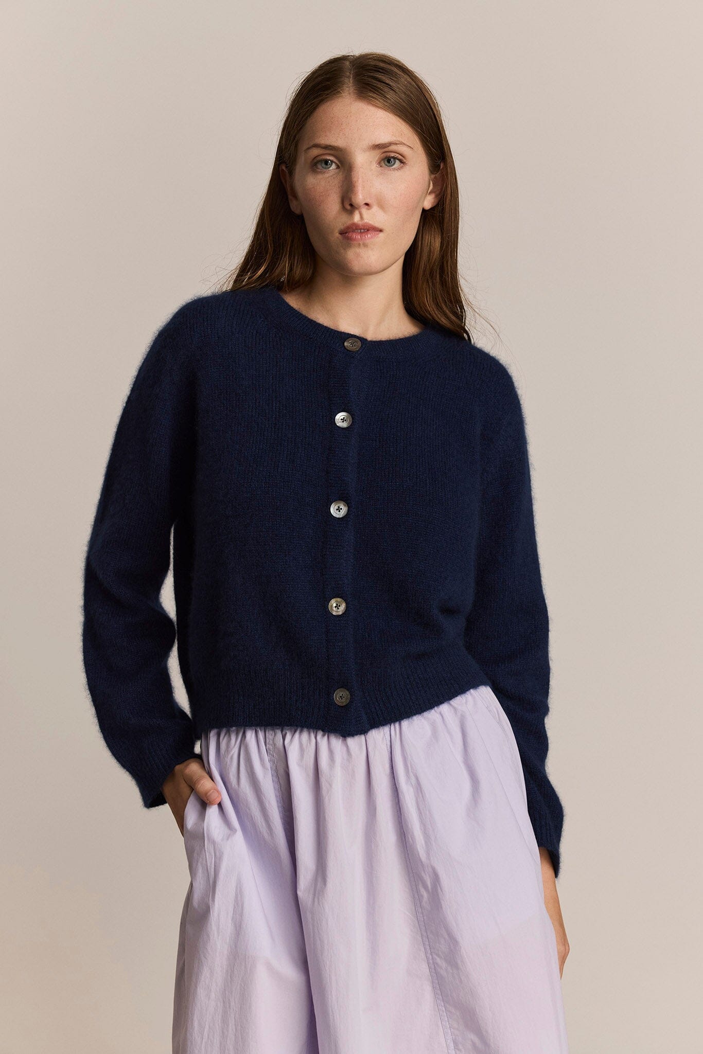 Woman wearing a navy cardigan with mother of pearl buttons against a beige background