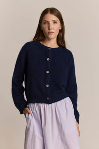 Woman wearing a navy cardigan with mother of pearl buttons against a beige background