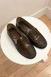 Pair of brown leather loafers on a white round table with a wooden floor background