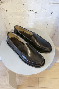 Pair of black loafers on a white round table with a light wood floor and white brick wall background.