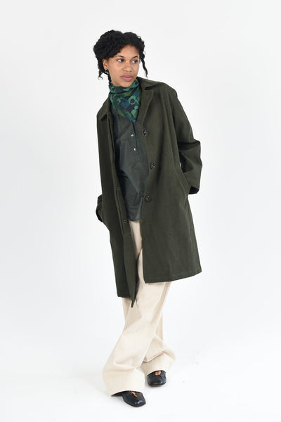 A woman wears the M.Patmos Slyvie MacKintosh jacket in 100% cotton. The color is forest green. The jacket has two pockets and buttons in the front. 