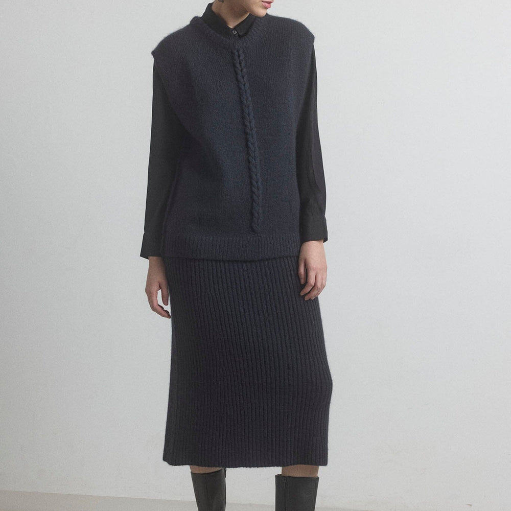
                  
                    Woman wearing a black knit outfit with the M.PATMOS Leigh cable vest and knit merino skirt on a white background
                  
                