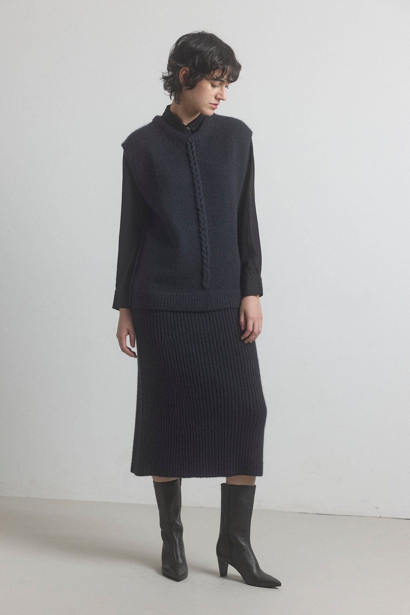 Woman wearing a black knit outfit with the M.PATMOS Leigh cable vest and knit merino skirt on a white background