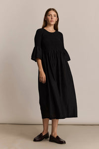 Woman wearing a black dress with ruffled bell sleeves against a beige background