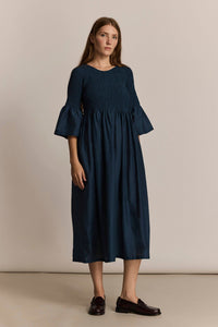 Woman wearing a dark blue dress with ruffled sleeves against a beige background