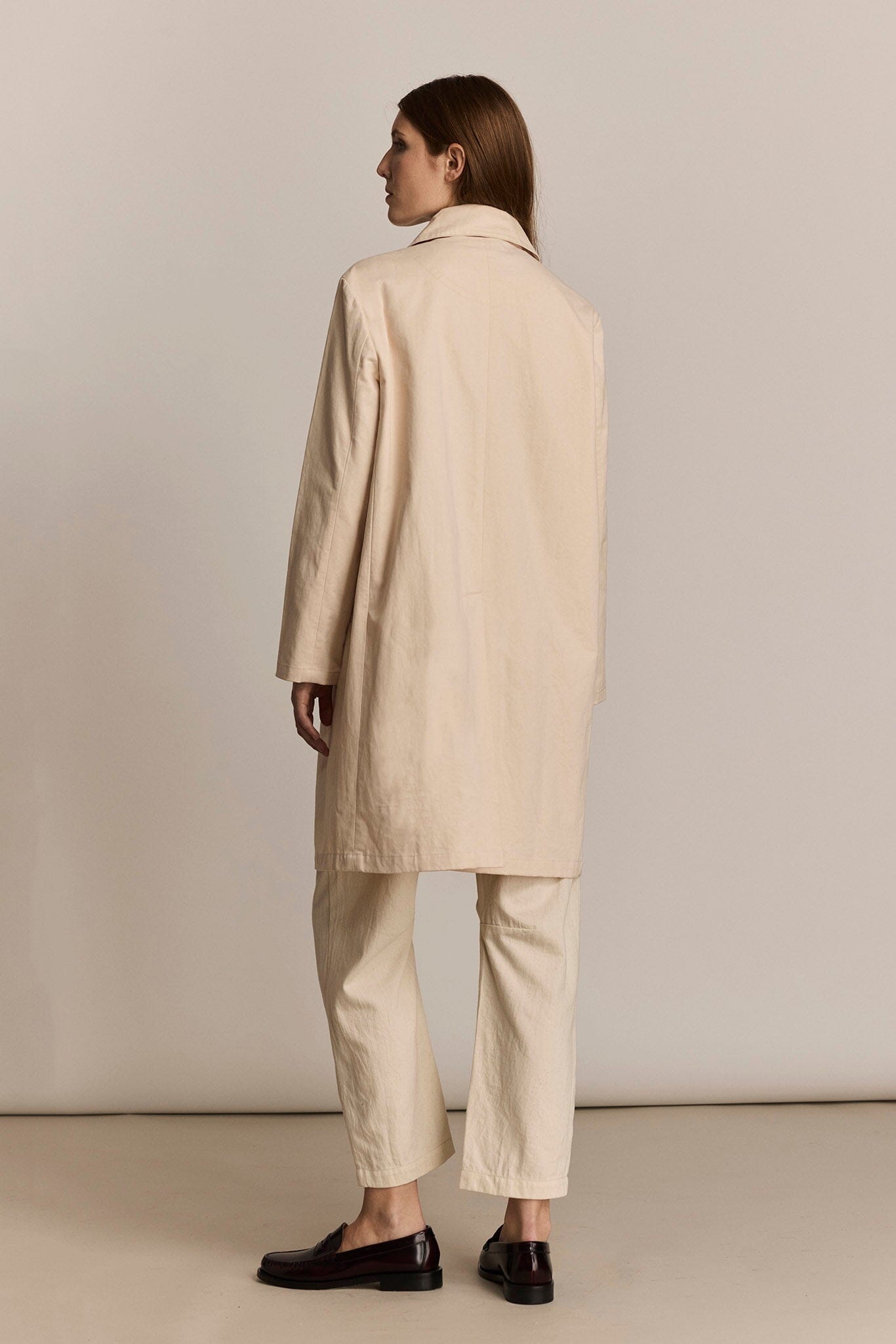 Woman wearing a beige coat and pants against a plain background