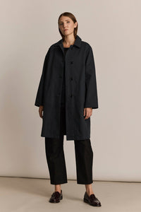 Woman wearing a charcoal trench coat and pants on a beige background