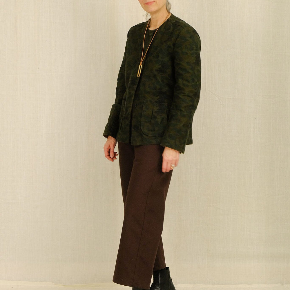 Woman wearing a green textured blazer and brown cotton pants against a plain background