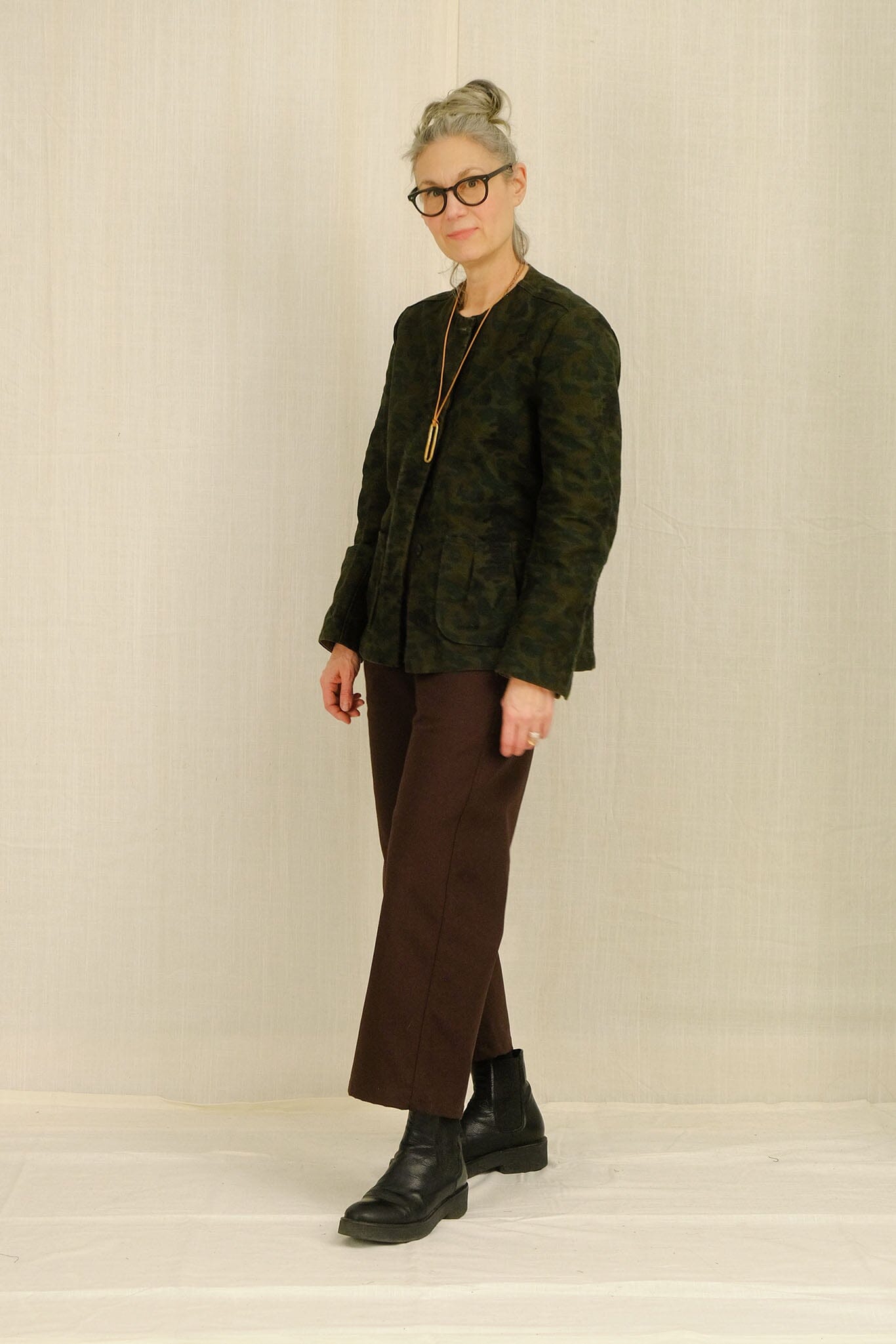 Woman wearing a green textured blazer and brown cotton pants against a plain background