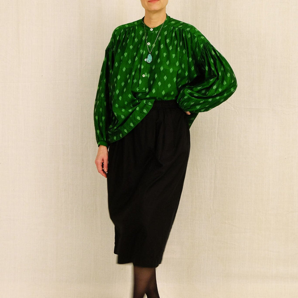 Woman wearing a green patterned blouse and black skirt against a plain background