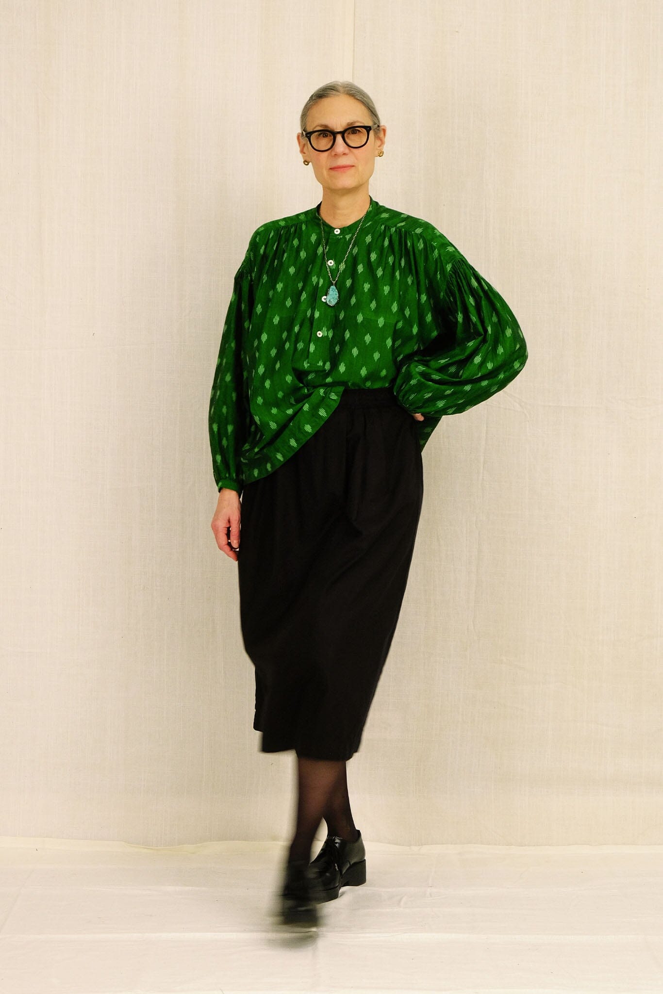 Woman wearing a green patterned blouse and black skirt against a plain background