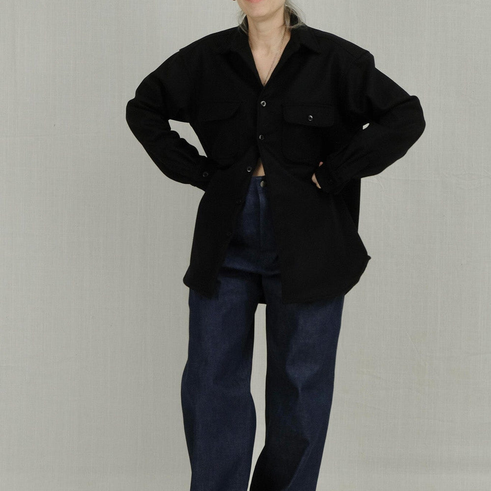 Woman wearing a black jacket and blue cuffed jeans on a plain background