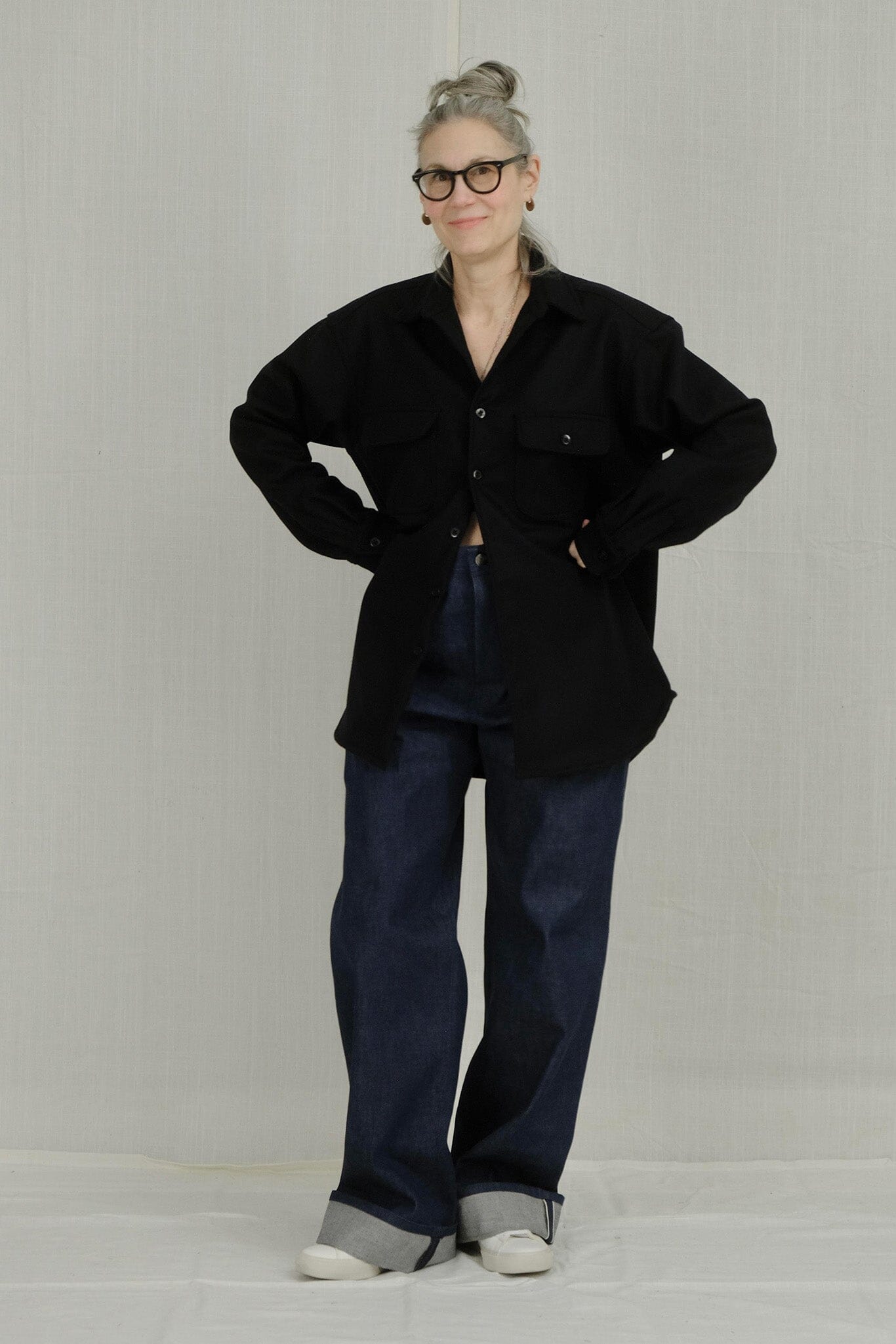 Woman wearing a black jacket and blue cuffed jeans on a plain background