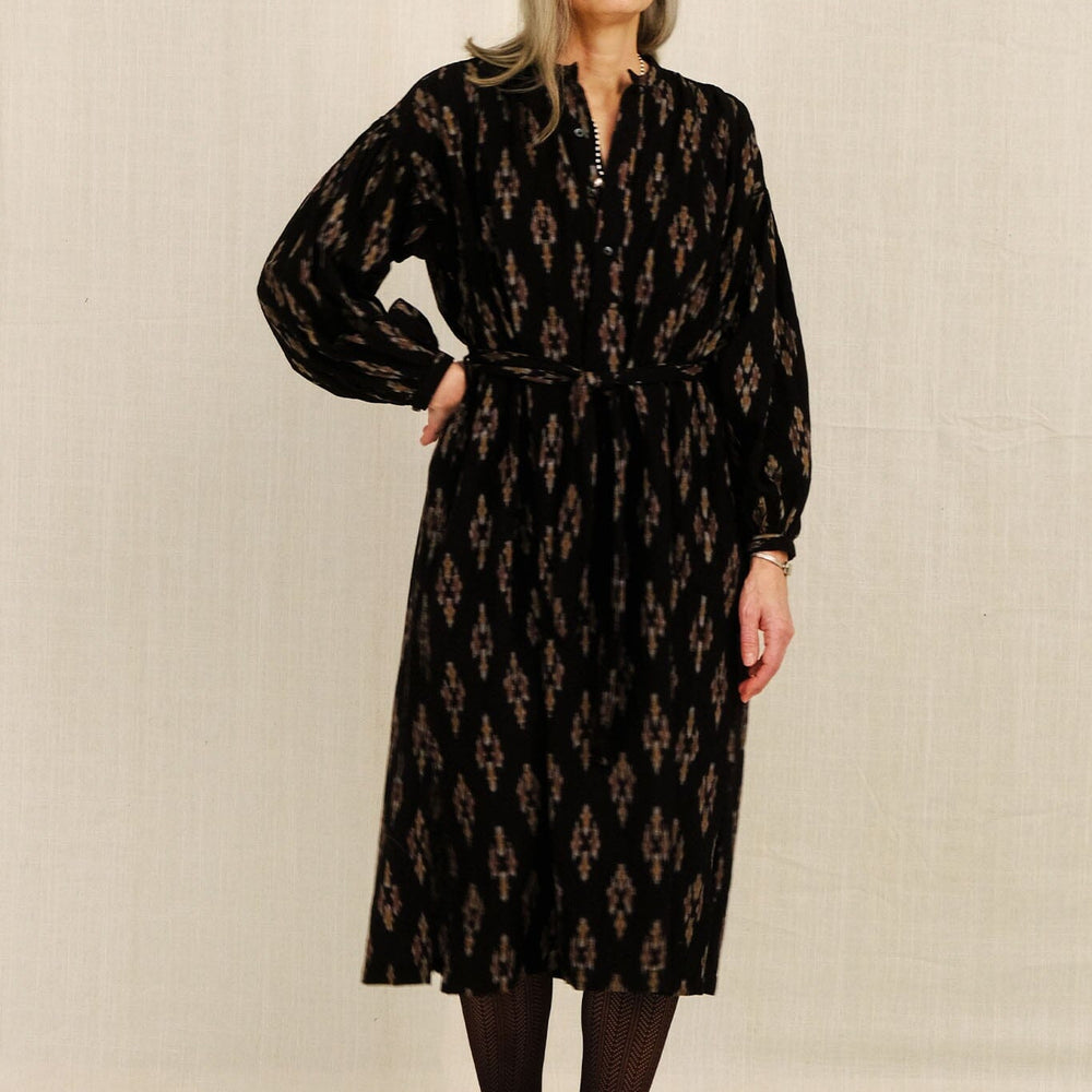 Woman wearing a black patterned long dress against a plain background
