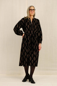 Woman wearing a black patterned long dress against a plain background