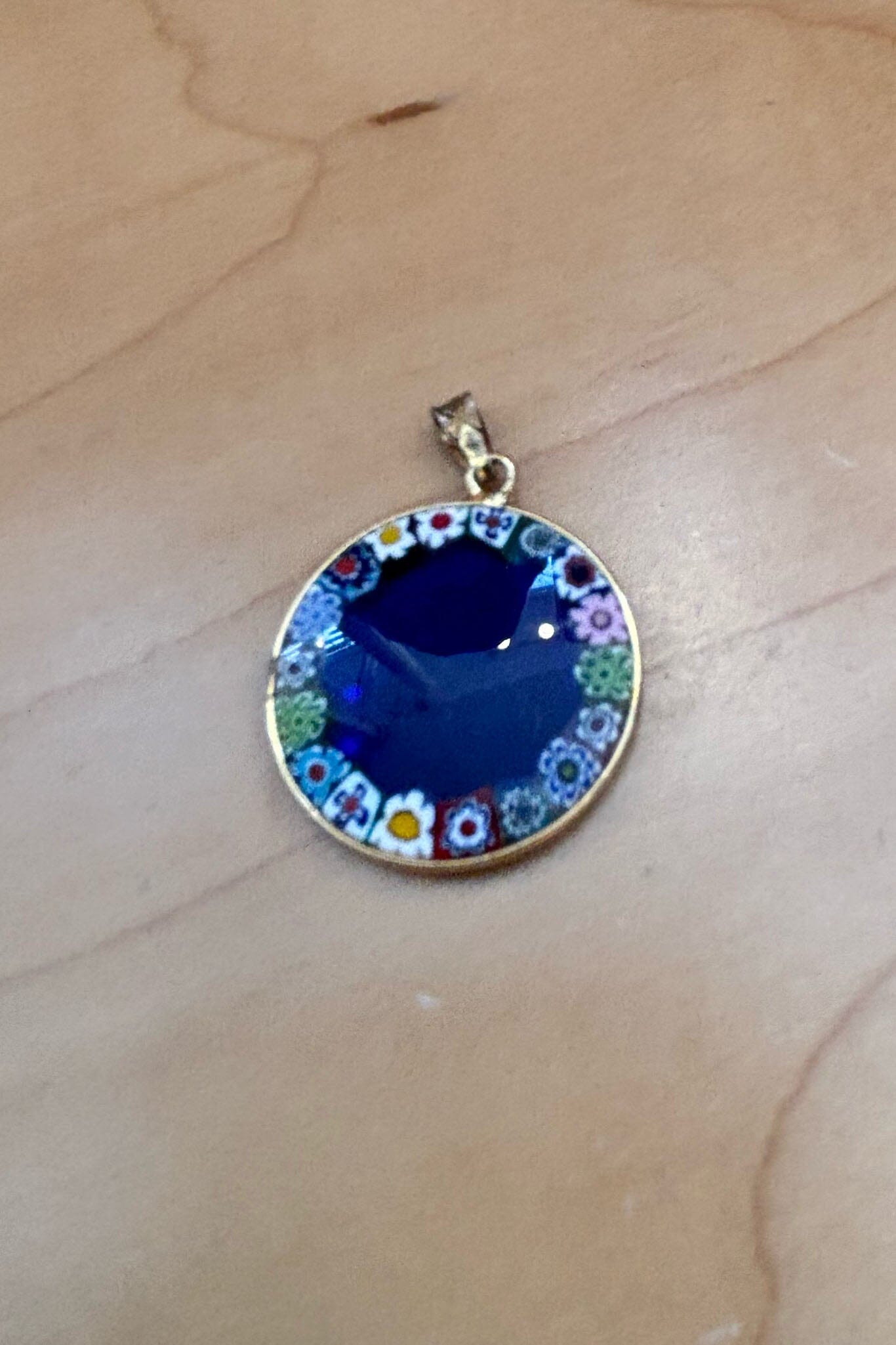 Round multicolored glass pendant with blue center on a light skin surface