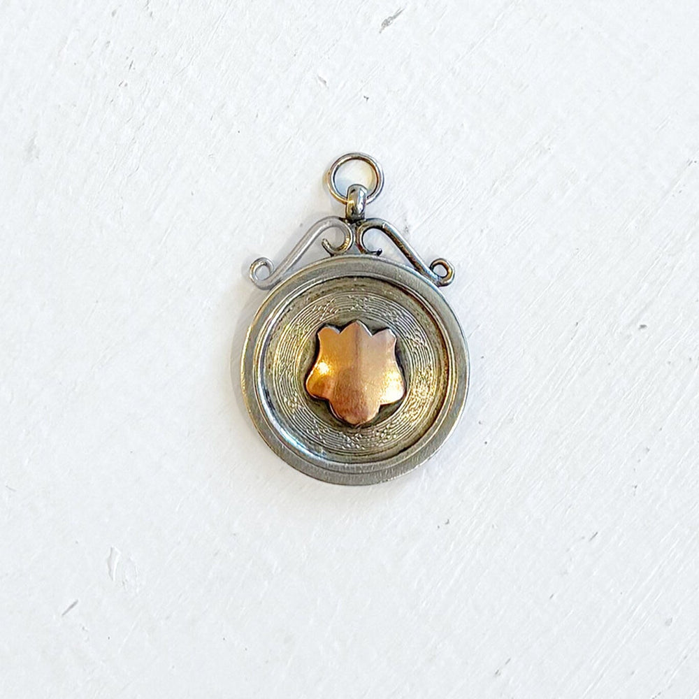 Vintage sterling silver pendant with a central rose gold shield emblem on a white background