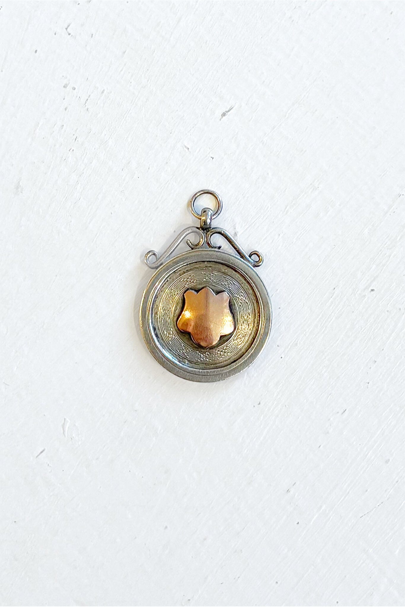 Vintage sterling silver pendant with a central rose gold shield emblem on a white background