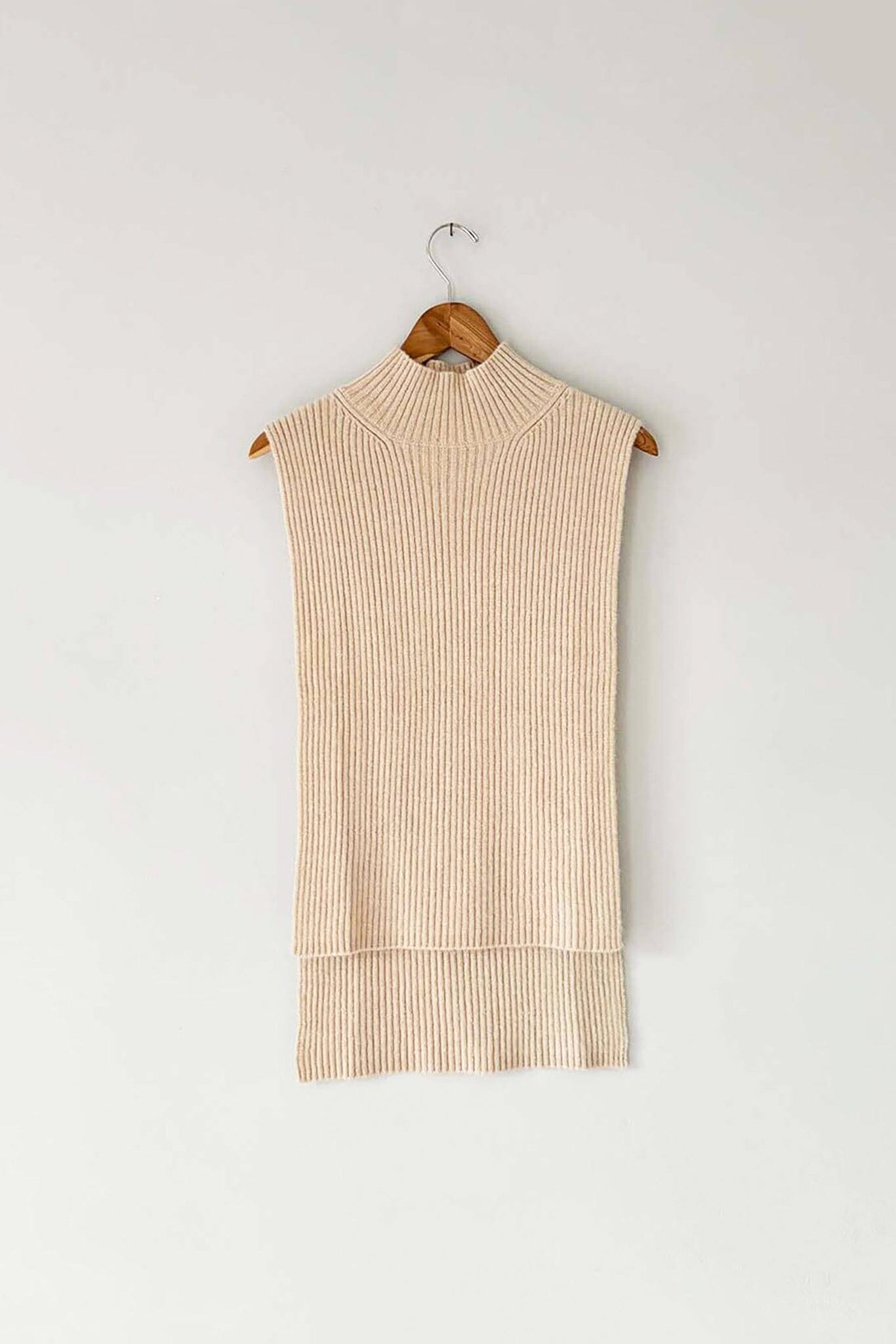 A beige, ribbed wool and cashmere blend vest with a mock funnel neck and high low hemline, displayed on a wooden hanger.