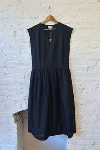 Black sleeveless dress on a hanger against a white brick wall.