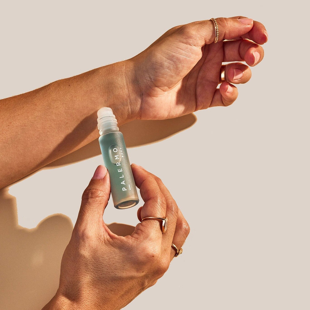 A person's hands holding a small bottle of Tranquility Aromatherapy Oil, with the cap off, dispensing the oil onto the skin.