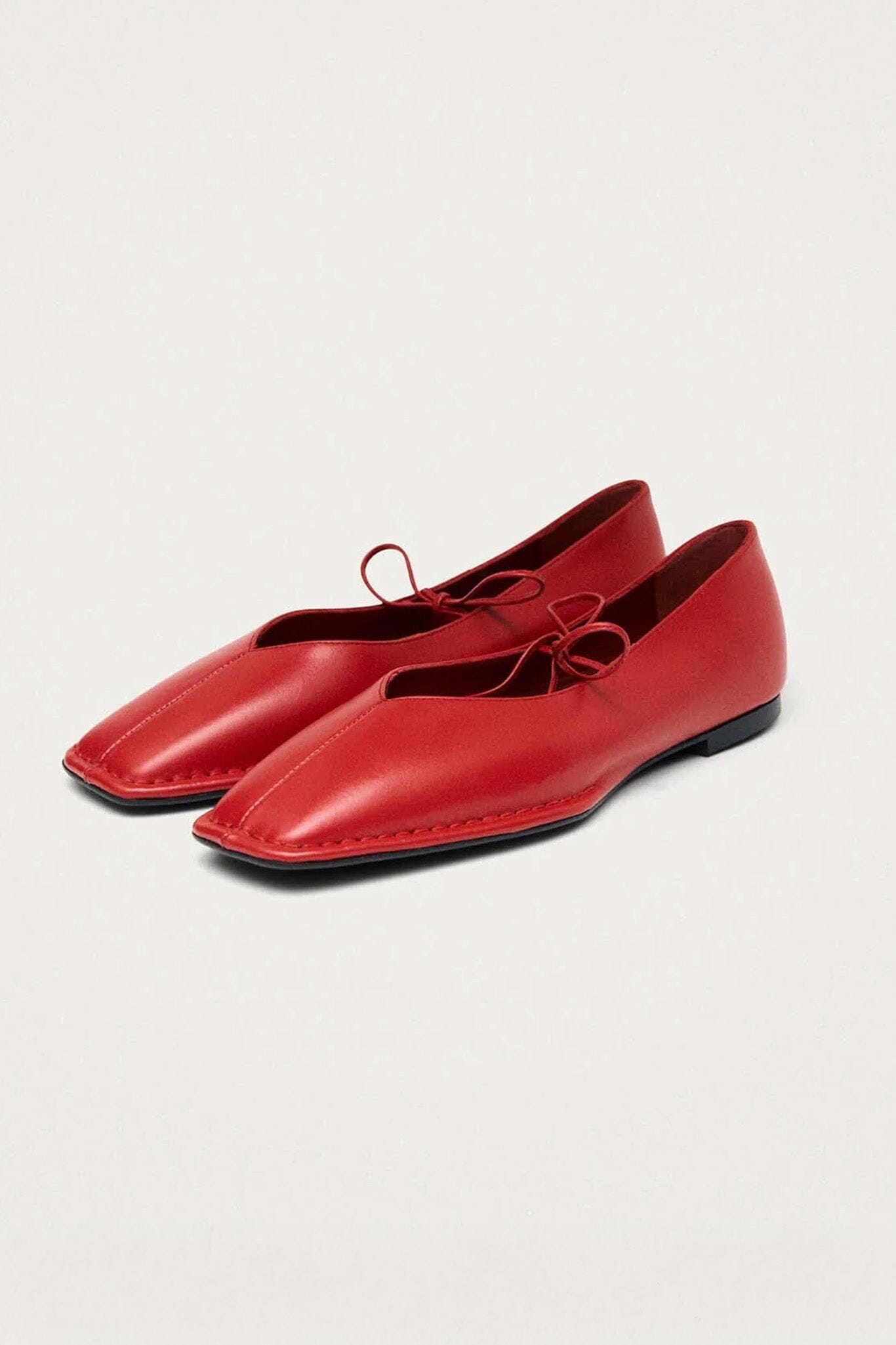 Side profile of red leather ballet flats on a light gray background