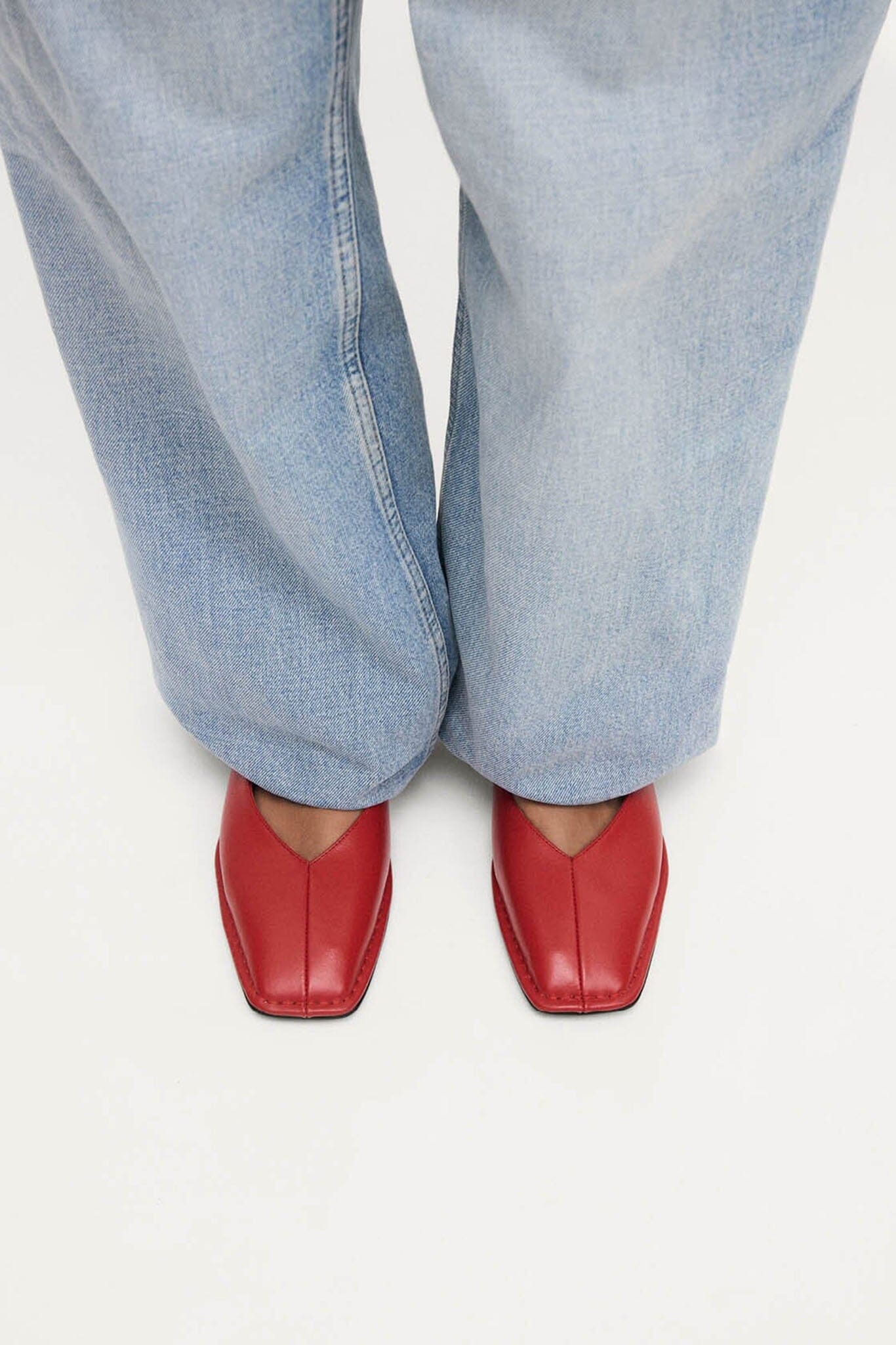 Red Alohas ballet flats worn with light blue jeans on a white background