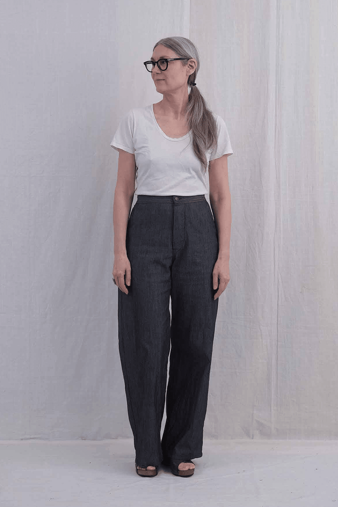 Person wearing a white t-shirt and high waisted denim pants against a plain background