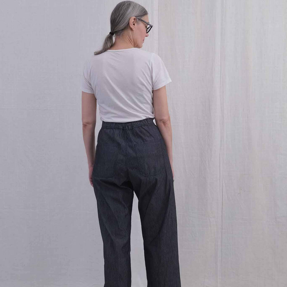 The back view of a woman wearing a white t-shirt and high waisted denim pants against a plain background