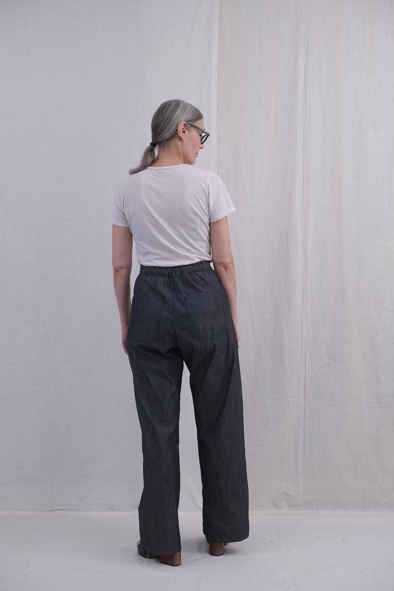 The back view of a woman wearing a white t-shirt and high waisted denim pants against a plain background
