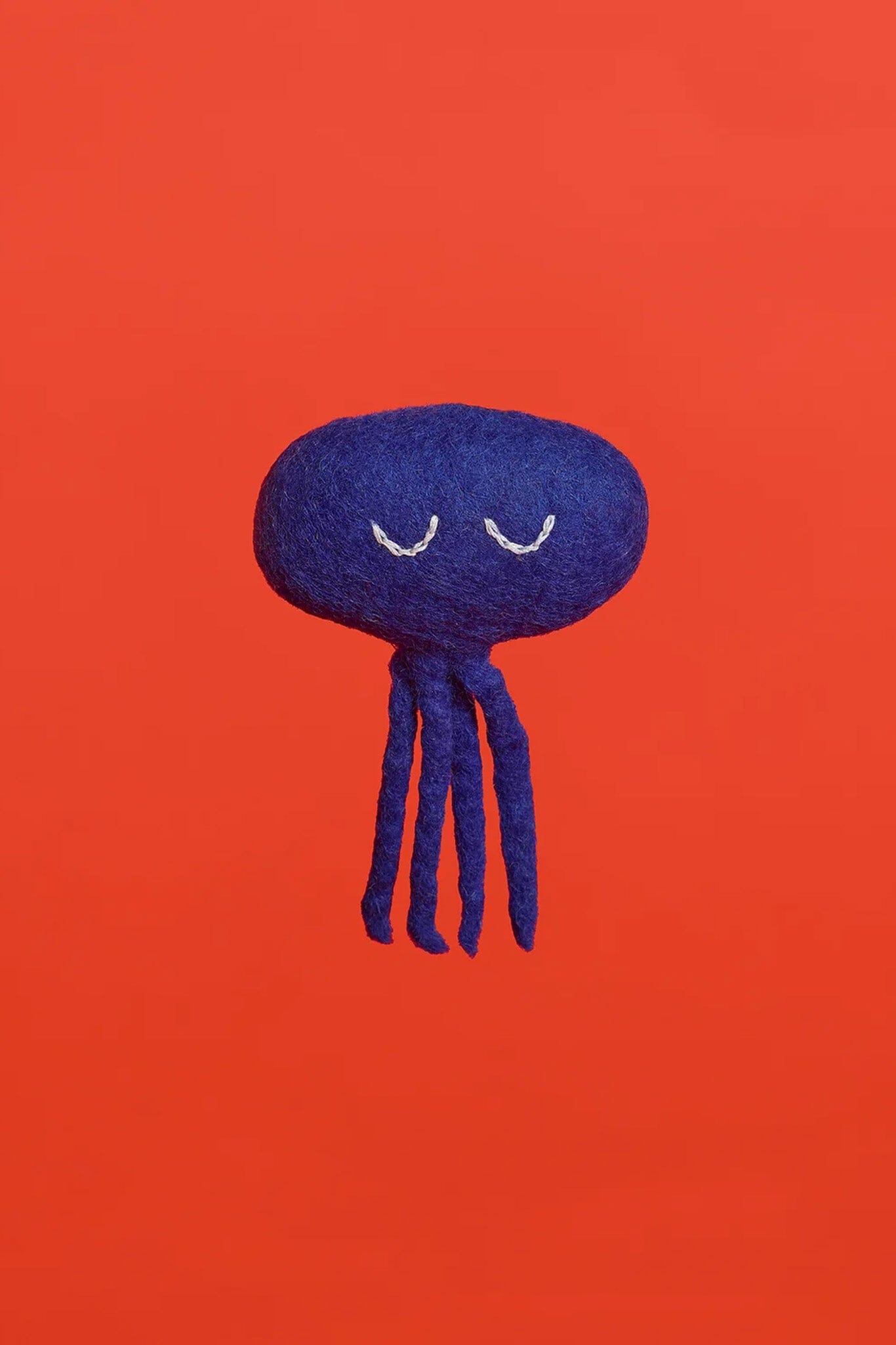 A blue octopus cat toy made of wool, displayed against a red background.