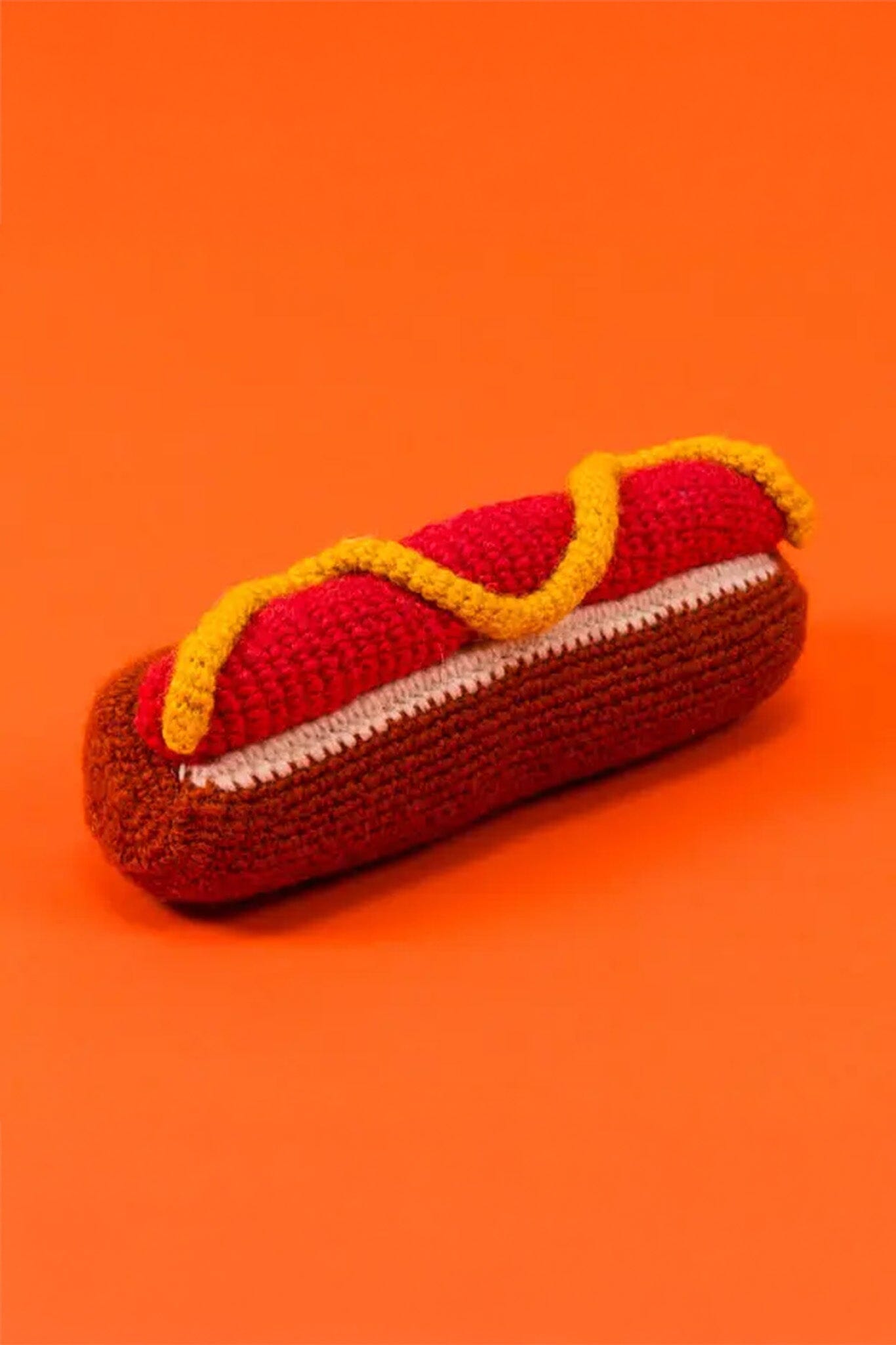 Crocheted hot dog toy on an orange background
