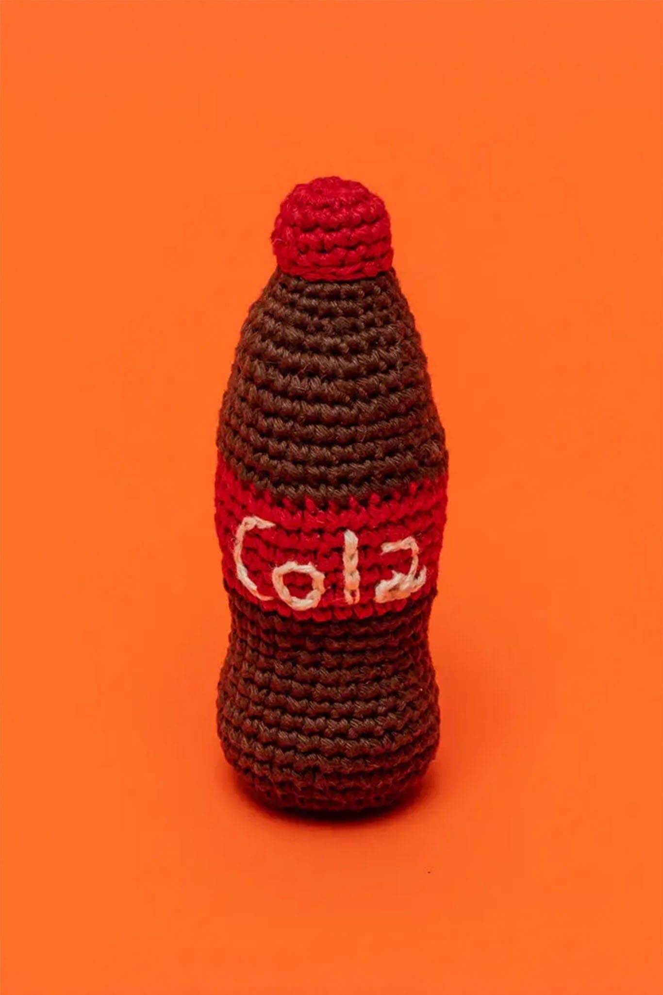Crocheted dog toy shaped like a Coca-Cola bottle on an orange background