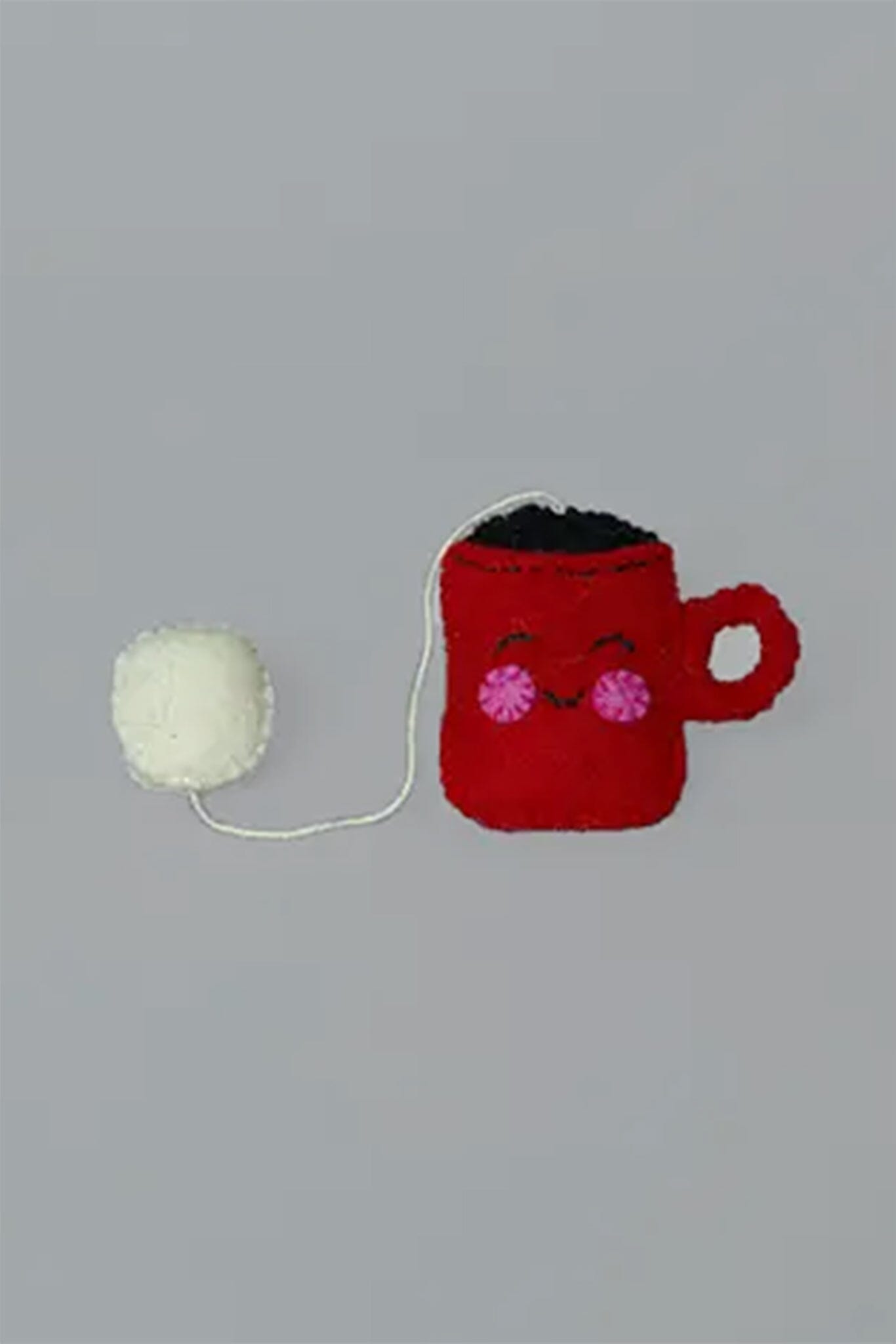 Red mug with a face and white yarn ball on a gray background