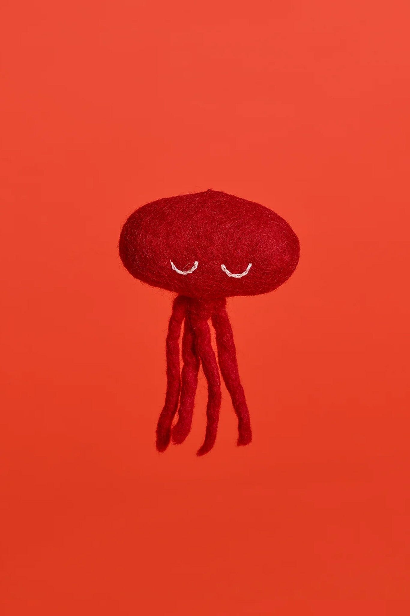 A red octopus-shaped cat toy made of wool, displayed on a red background.