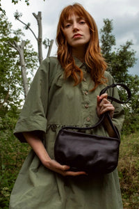 Model holding the Kate Sheridan Black Mini Eve Bag outdoors. A stylish, UK-designed everyday black leather handbag.