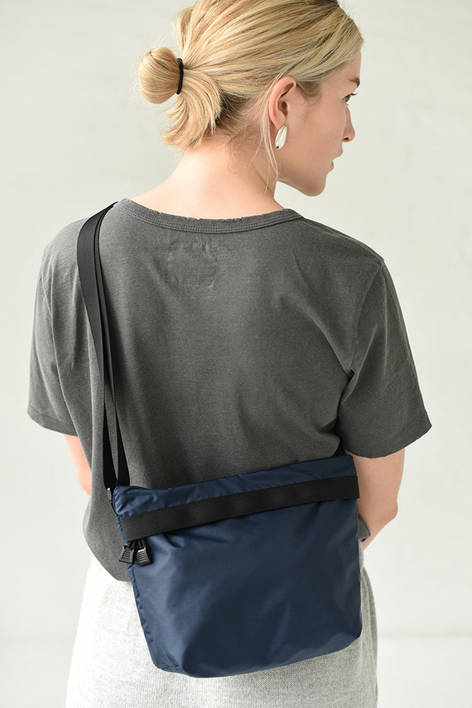 
                  
                    A person wearing a navy nylon crossbody bag with a visible zipper and two interior pockets. The bag is lightweight and water resistant.
                  
                