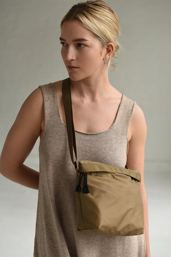 
                  
                    Woman wearing a crossbody waterproof zipper bag in a light green and brown color.
                  
                