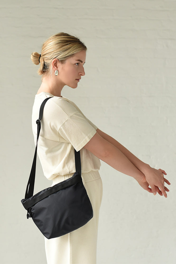 
                  
                    The side view of a woman wearing a black square crossbody bag
                  
                