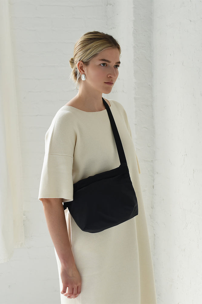 
                  
                    A woman in a cream short sleeve dress wearing a black crossbody zipper bag
                  
                