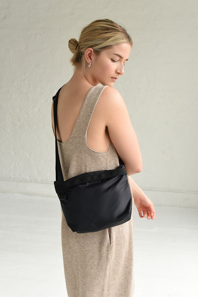 
                  
                    A person wearing a beige dress is seen from behind, carrying a black nylon crossbody bag with a crossbody shoulder strap.
                  
                