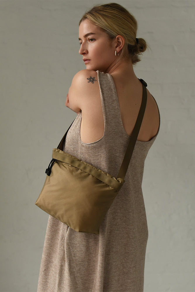 
                  
                    A woman wearing a square crossbody zipper bag in a light brown. 
                  
                