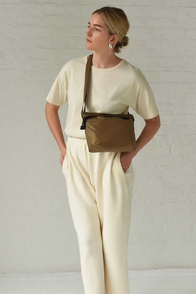 A person wearing a beige outfit carrying a light brown nylon crossbody bag.