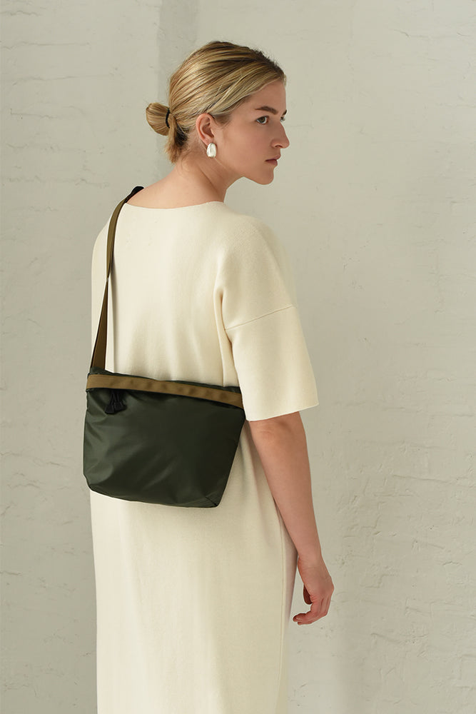 A woman wearing a white dress is seen from behind, carrying an olive green nylon crossbody bag with a shoulder strap.