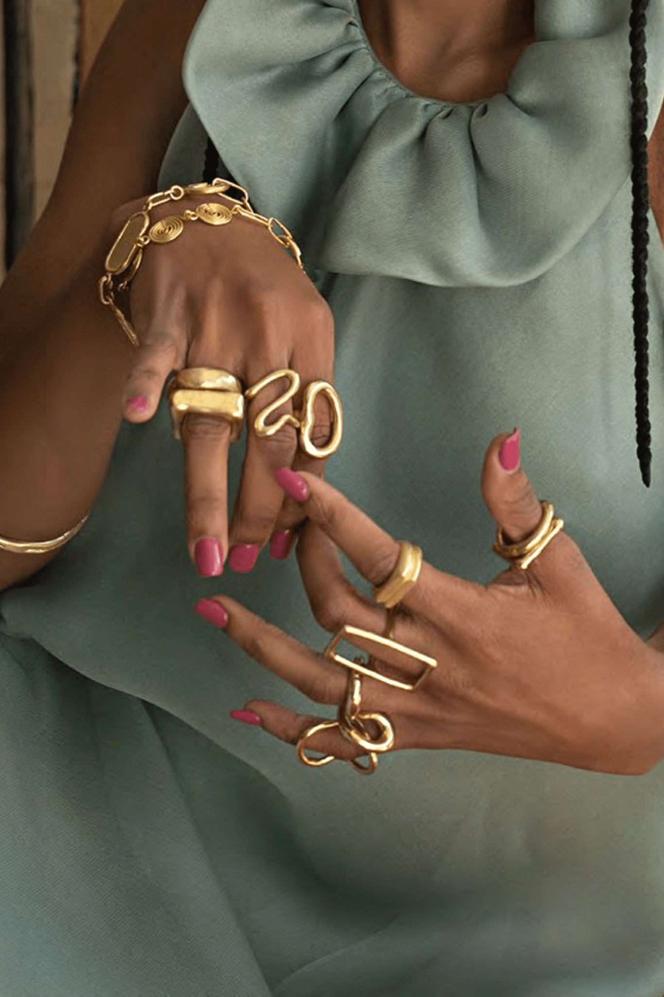 A woman in a green dress wears many gold brass rings on her fingers. 