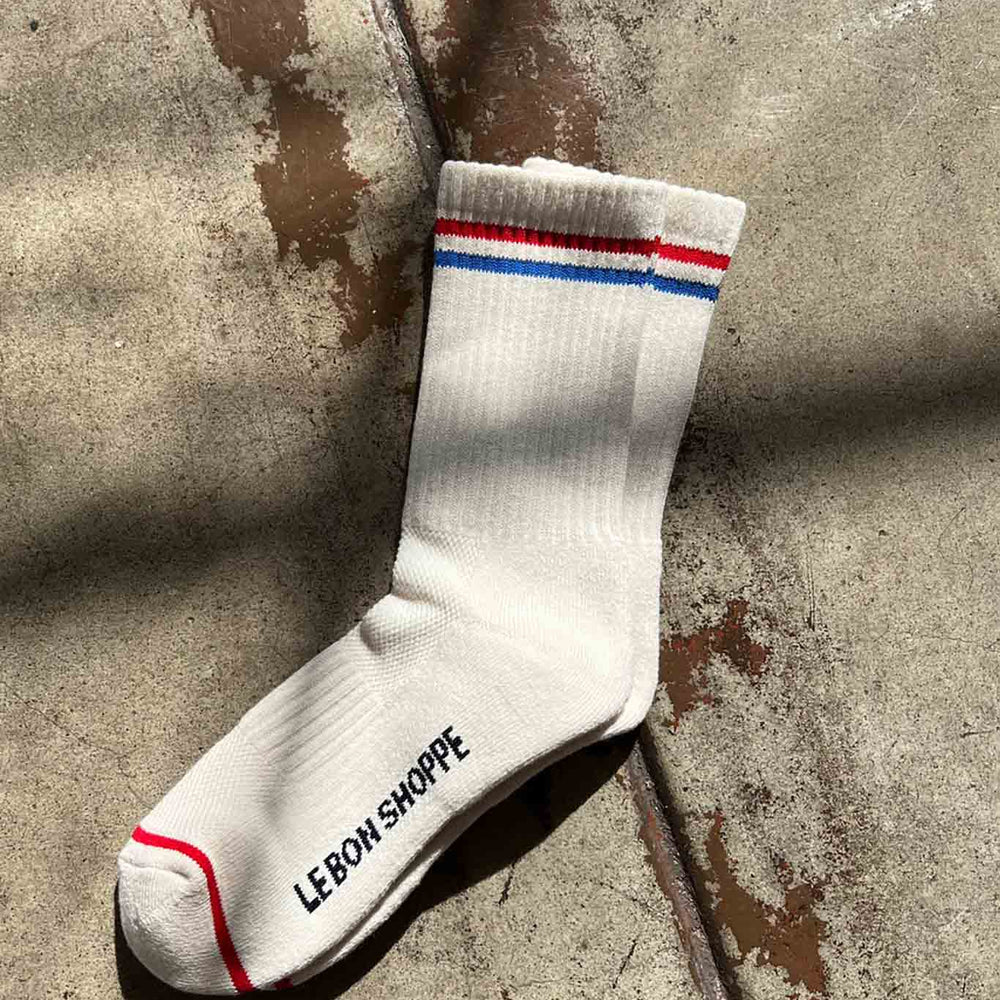 Off white ribbed cotton socks with a red and blue top stripe a logo on the bottom