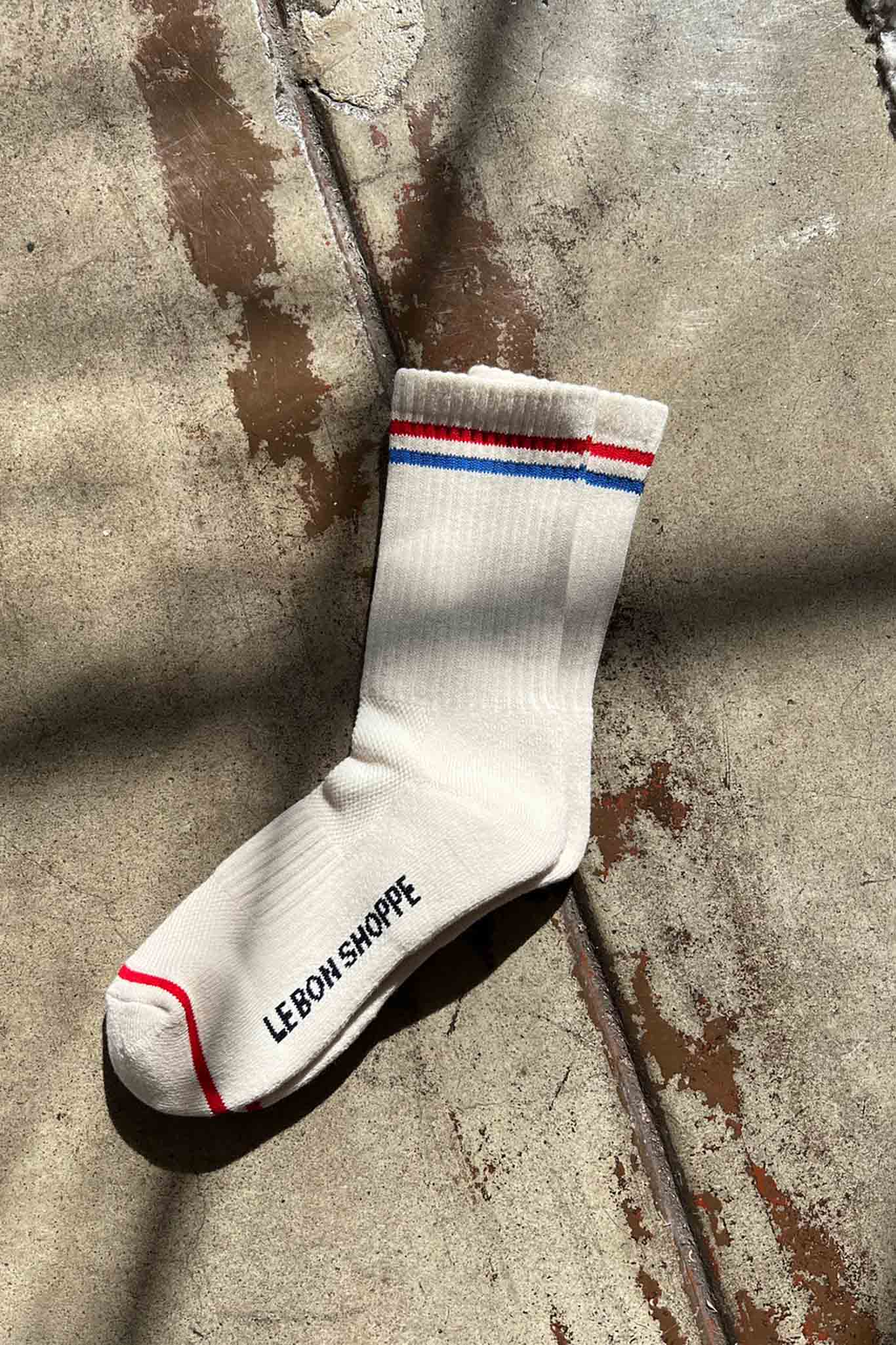 Off white ribbed cotton socks with a red and blue top stripe a logo on the bottom